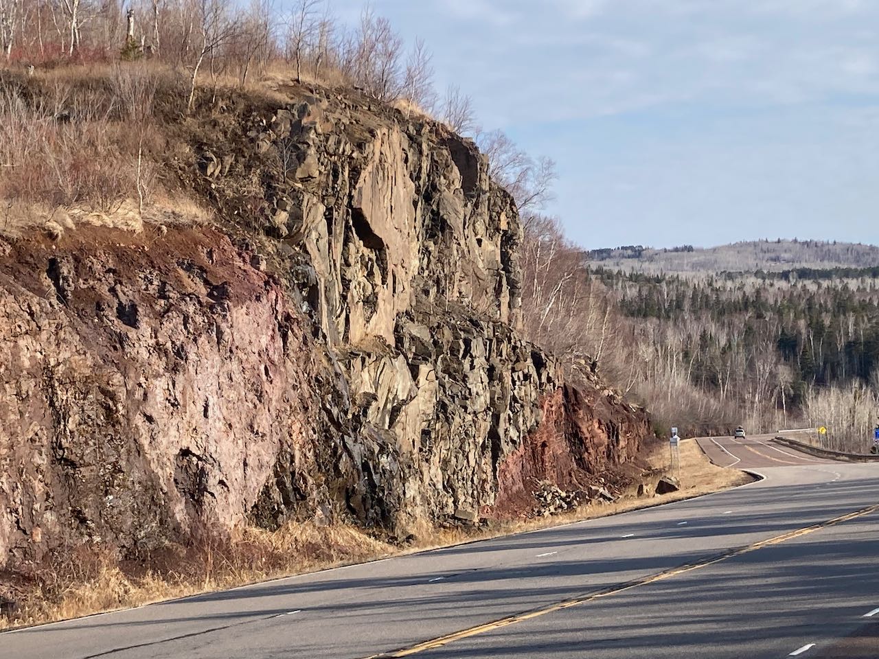 Roadside with Cutface cliff on one side and a forested area on the other, under a clear blue sky.
